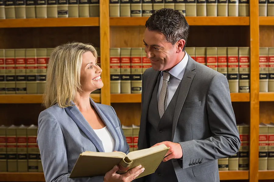 Two legal professionals discussing reference materials in a law library — representing how attorneys’ professional experience, legal knowledge, and individual reputations contribute to their firm’s visibility in search and AI engines.